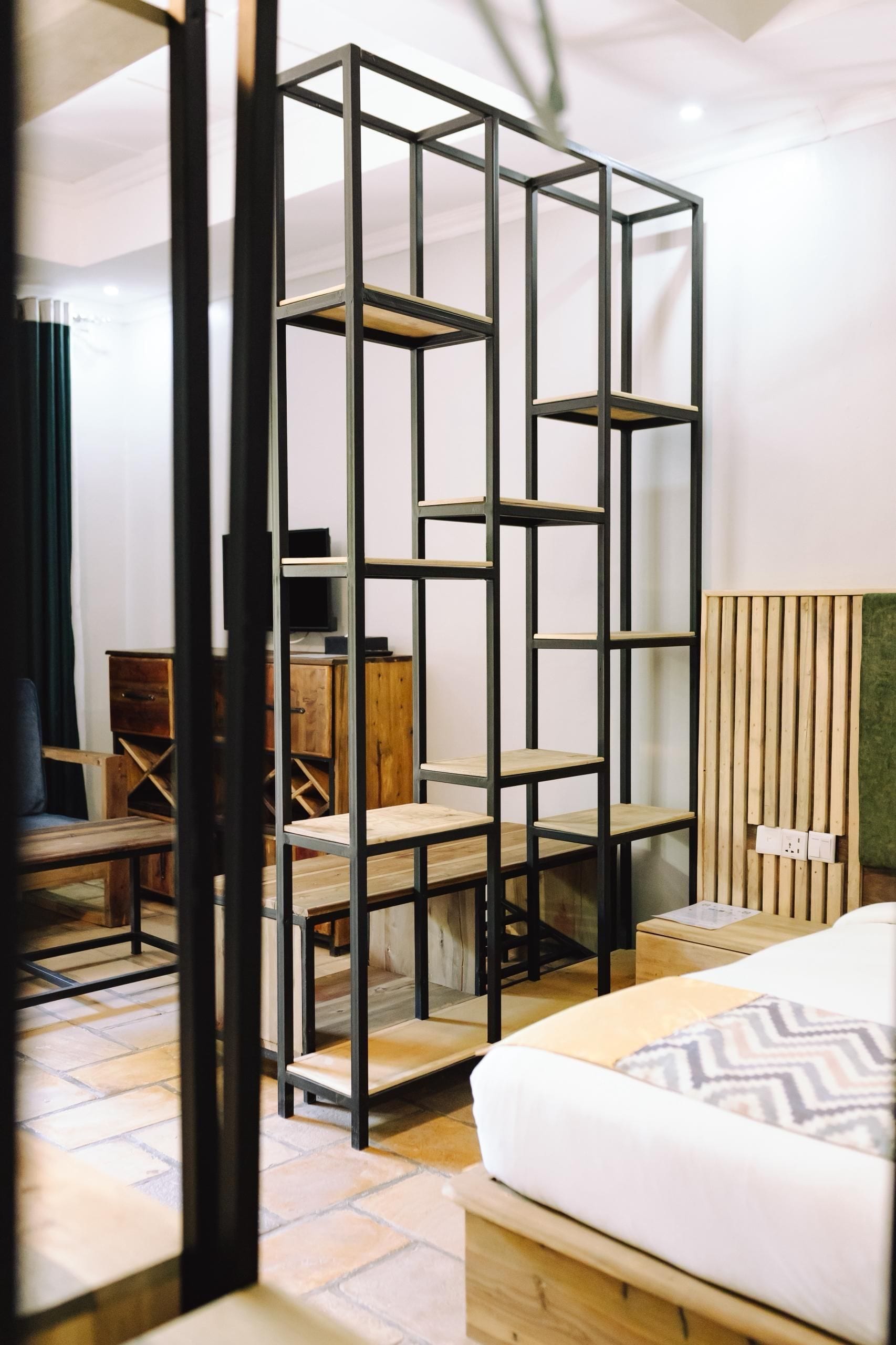A modern bedroom with a bed, a wooden bedside table, a black metal shelving unit, and a wooden slatted wall panel.