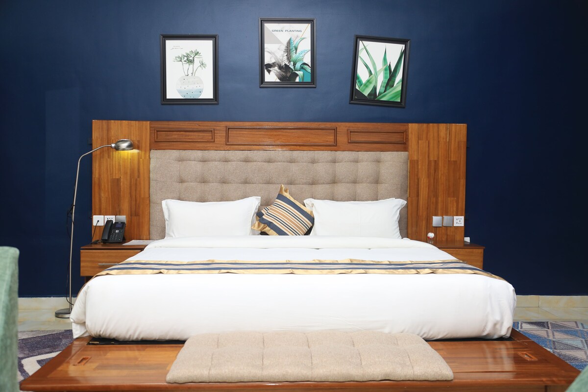 A bedroom with a wooden headboard, a bed with white bedding, a bedside lamp, and three framed botanical prints on the wall.