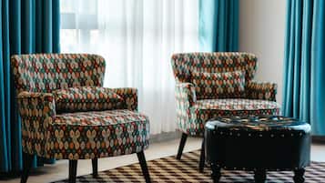 A living room with two patterned armchairs and a black ottoman on a patterned rug.