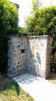 Zona de ducha exterior de piedra con suelo de hormigón, rodeada de follaje.