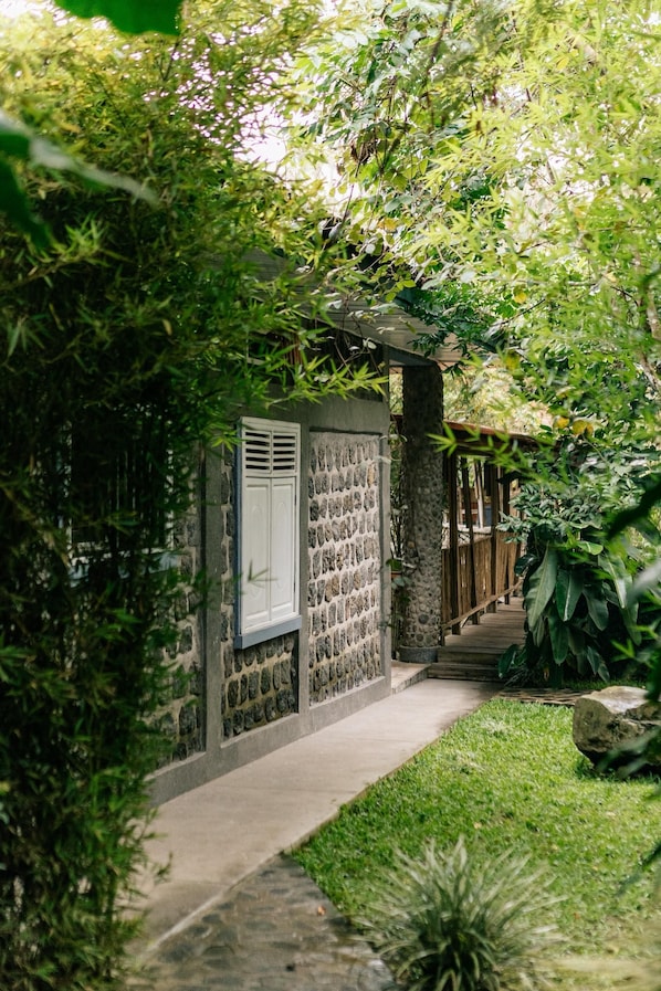 Un edificio de piedra con una ventana y una puerta, rodeado de abundante vegetación.