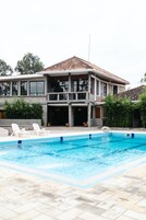 A two-story house with a swimming pool, a covered patio, and a view of the surrounding greenery.