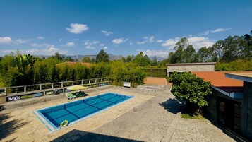 Una piscina con bordeado de azulejos, rodeada por una cerca y árboles, con montañas al fondo.