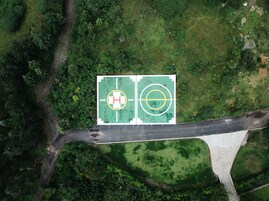 An aerial view of a basketball court with a hospital symbol, surrounded by dense greenery and a bridge.
