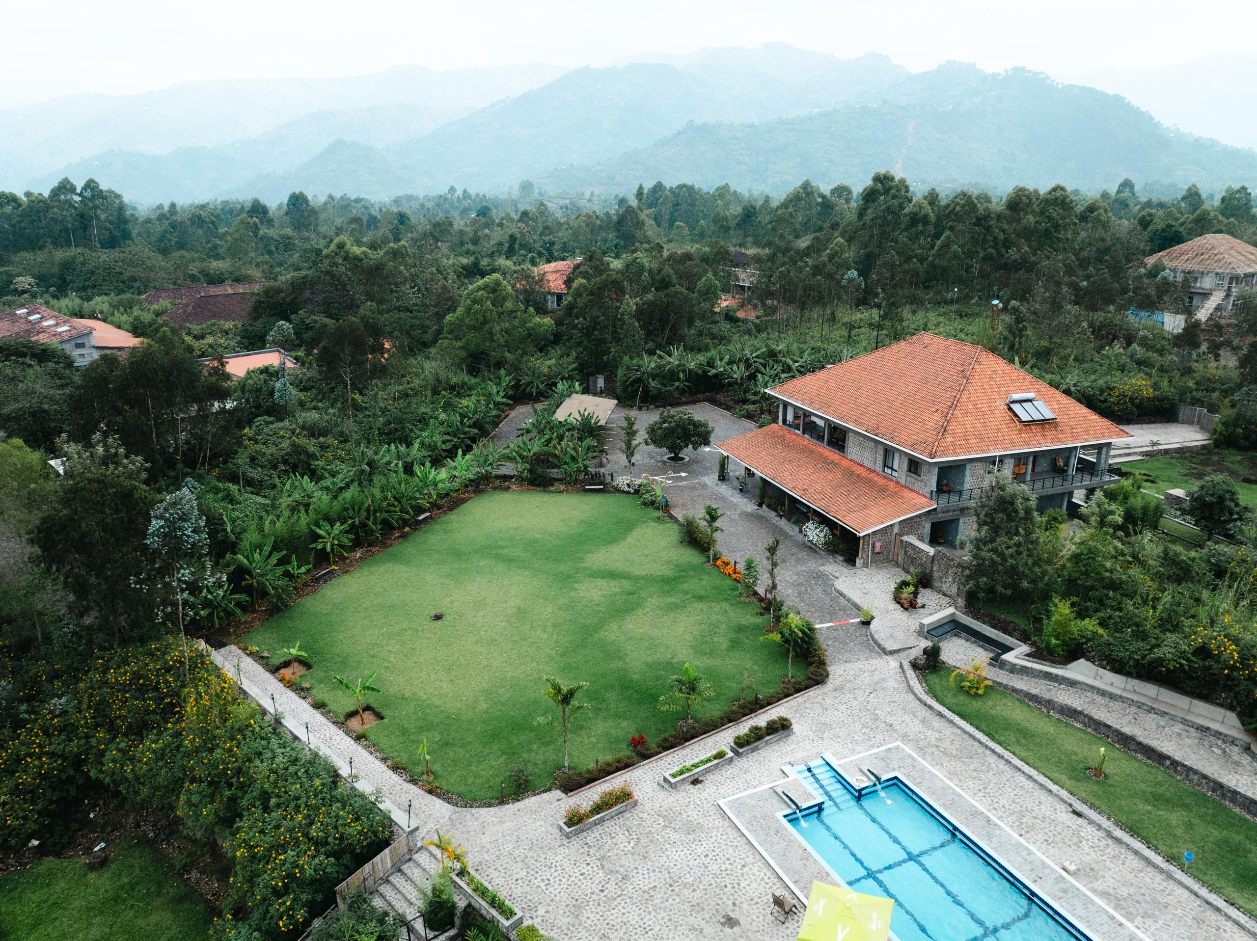 A large house with a swimming pool, surrounded by lush greenery and mountains in the background.