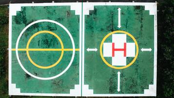 A basketball court with a hoop and a H symbol, surrounded by a green surface with white and yellow markings.