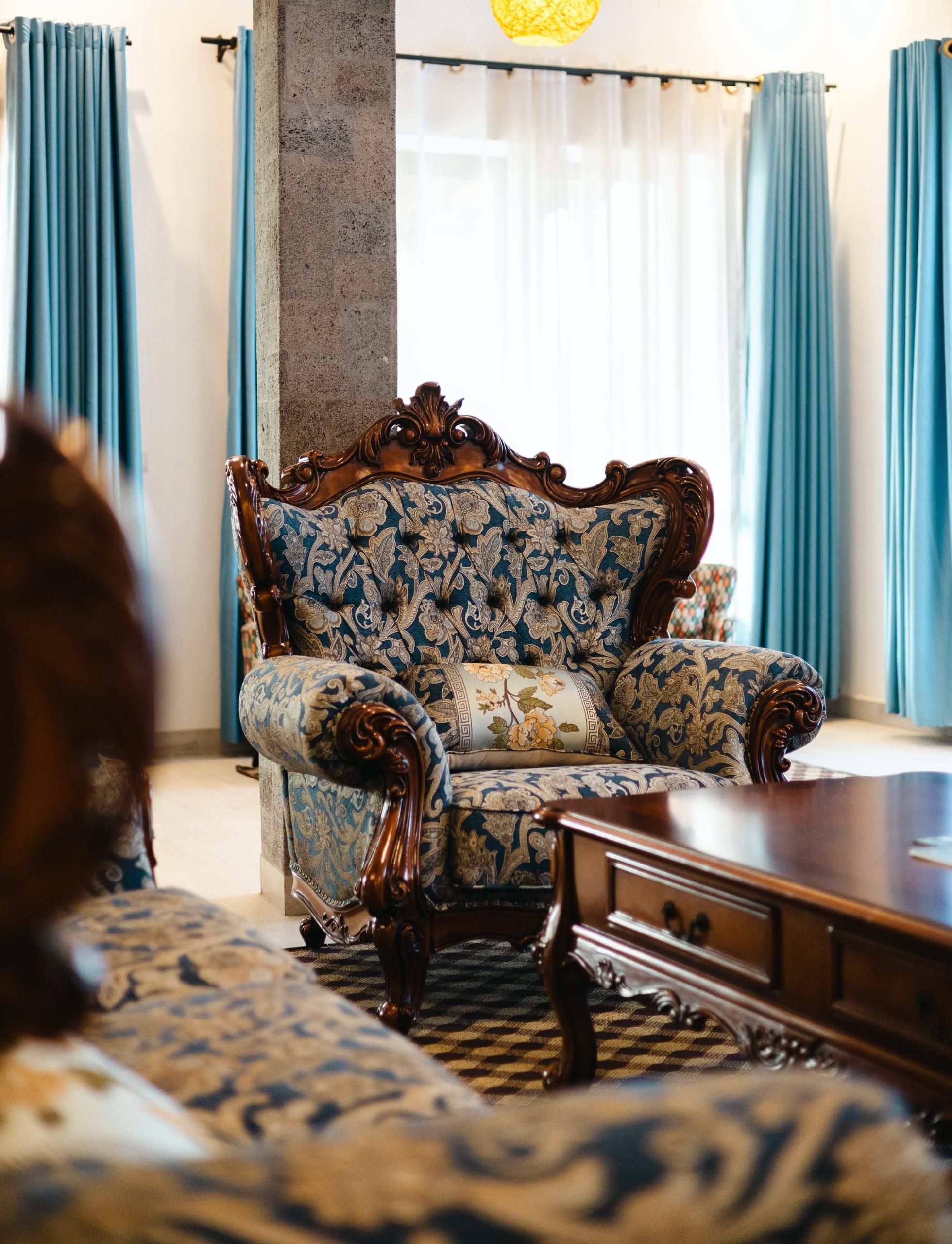 A room with a patterned sofa, a wooden coffee table, and a view of a building outside.
