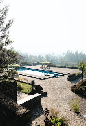 A swimming pool with lounge chairs and a covered area, surrounded by stone pathways and greenery. - Buhanga Eco Lodge (Nyakinama)