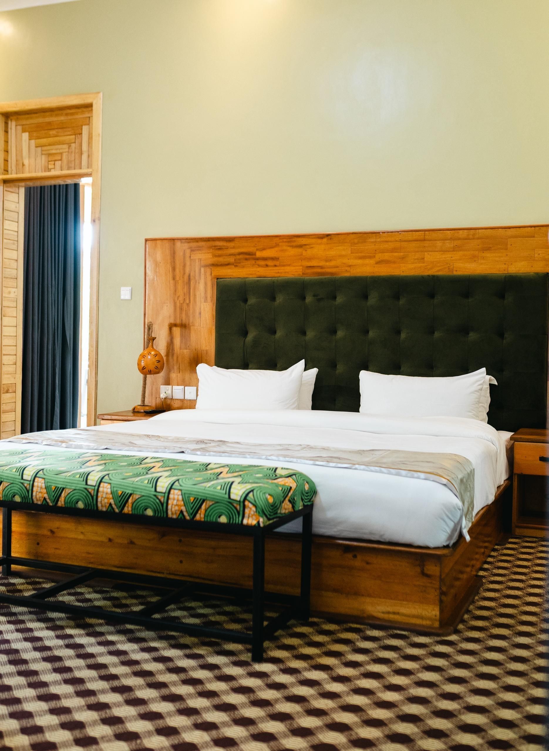 Habitación de hotel con una cama grande, cabecera de madera, suelo a cuadros y puerta de madera.
