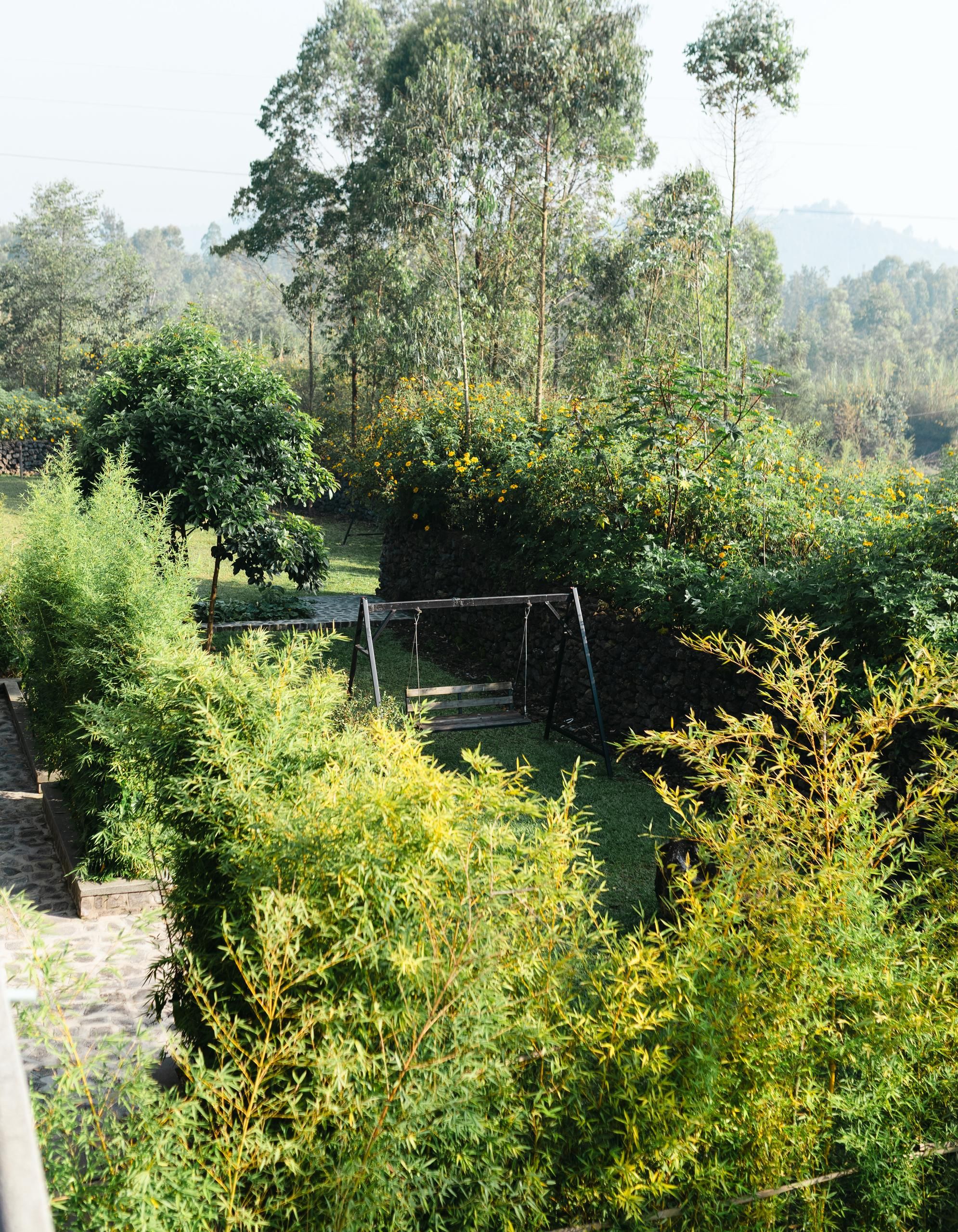 A garden with a wooden swing set, stone pathway, and various green shrubs.