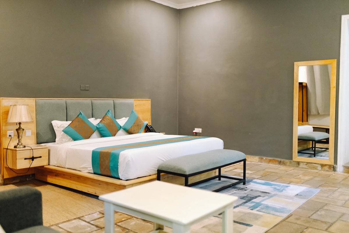Habitació d'hotel amb llit, taula de nit, làmpada, cadira i mirall.