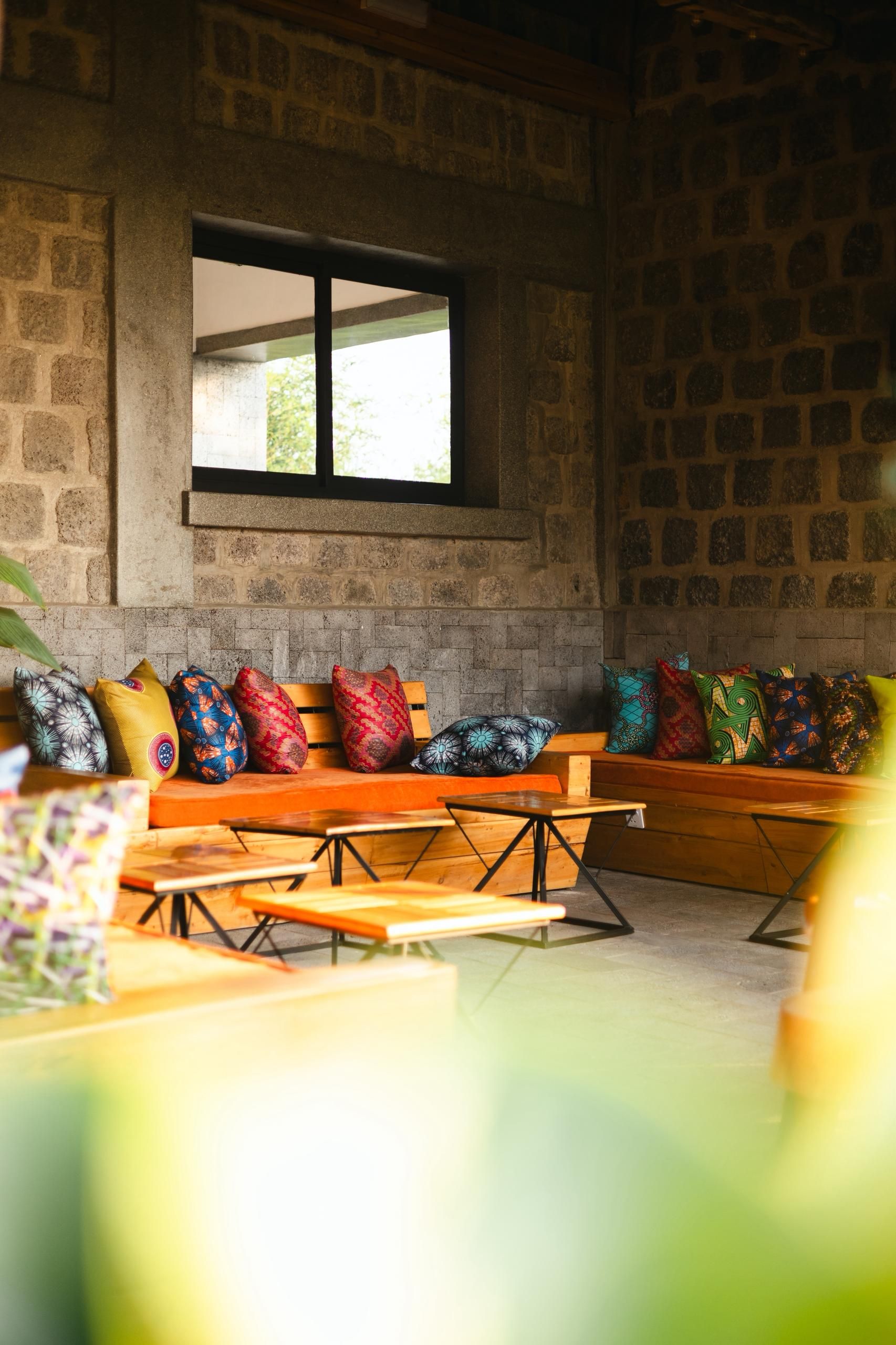 A rustic interior with stone walls, a wooden bench with colorful cushions, and a window providing natural light.