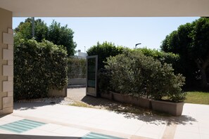 Un espace extérieur doté d’un chemin pavé, d’une entrée avec une porte en verre et de différents arbustes décoratifs.