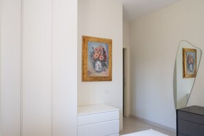 A minimalist room with a white dresser, a painting of flowers, and a mirror reflecting the room. - Villa Andrews by Wonderful Italy (Bari)
