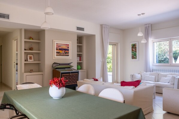 Un salon moderne avec un coin repas, des meubles blancs et des œuvres d’art accrochées aux murs.