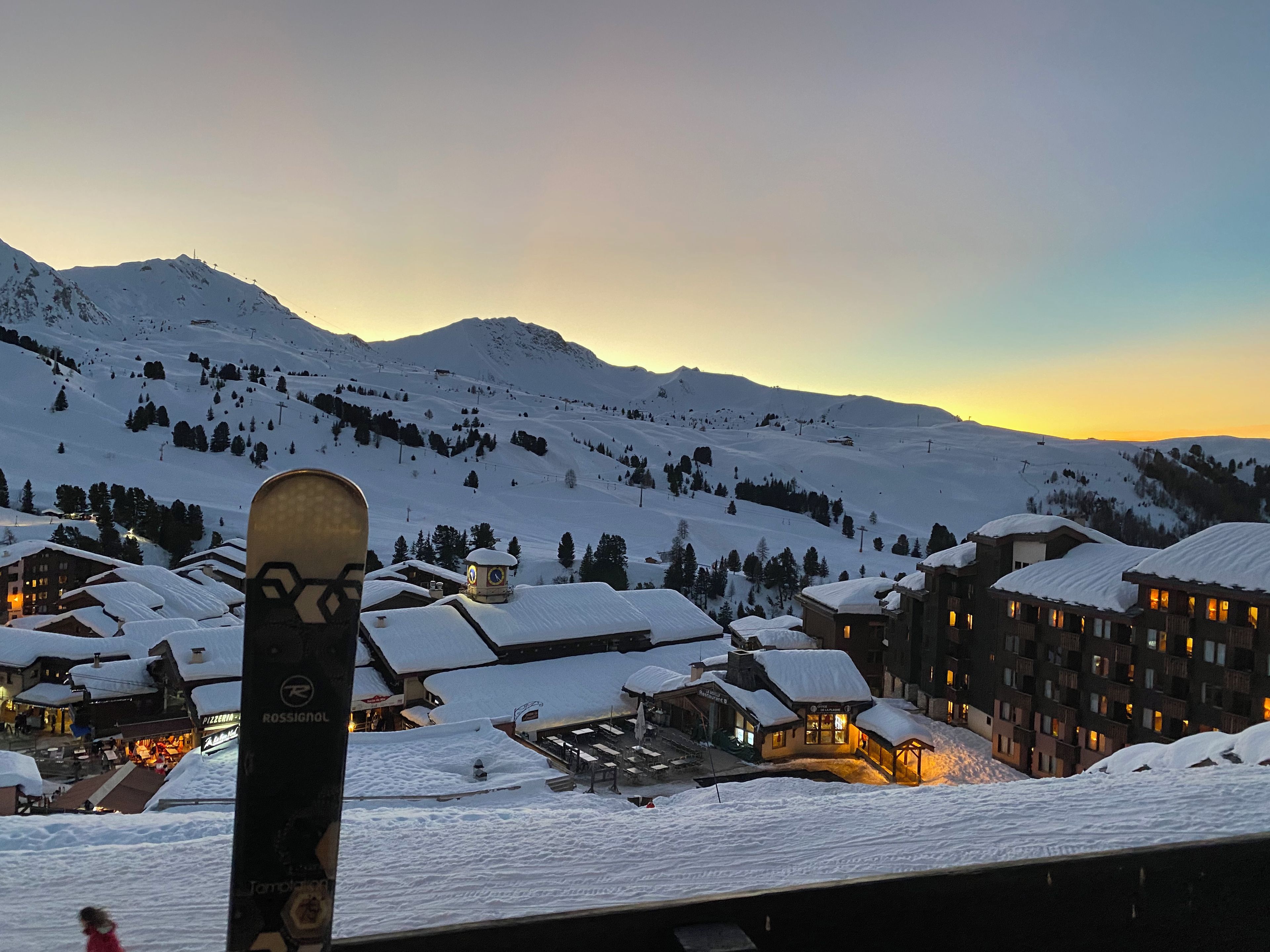 Un village de montagne enneigé, avec des bâtiments et un télésiège en arrière-plan.