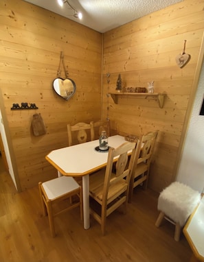 Ein Holzinnenraum mit einem Esstisch, Stühlen, einem hängenden herzförmigen Spiegel und einem kleinen Regal mit Dekorationen.