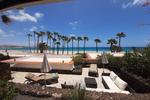 Ein Strand-Loungebereich mit Liegestühlen, Sonnenschirmen und Blick auf das Meer.