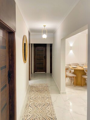 A hallway with a wooden door, a mirror, a patterned rug, a dining area with a round table and chairs, and a ceiling light fixture. - 3BRs Bohimian Citycenter Apartmemt (Cairo Governorate)