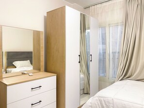 Ein Schlafzimmer mit einem Bett, einem Nachttisch, einem Spiegel, einem Kleiderschrank und einem Fenster mit Vorhängen.