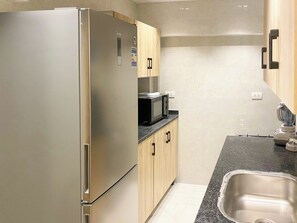 A compact kitchen with a stainless steel refrigerator, a microwave, wooden cabinets, and a stainless steel sink. - 3BRs Bohimian Citycenter Apartmemt (Cairo Governorate)
