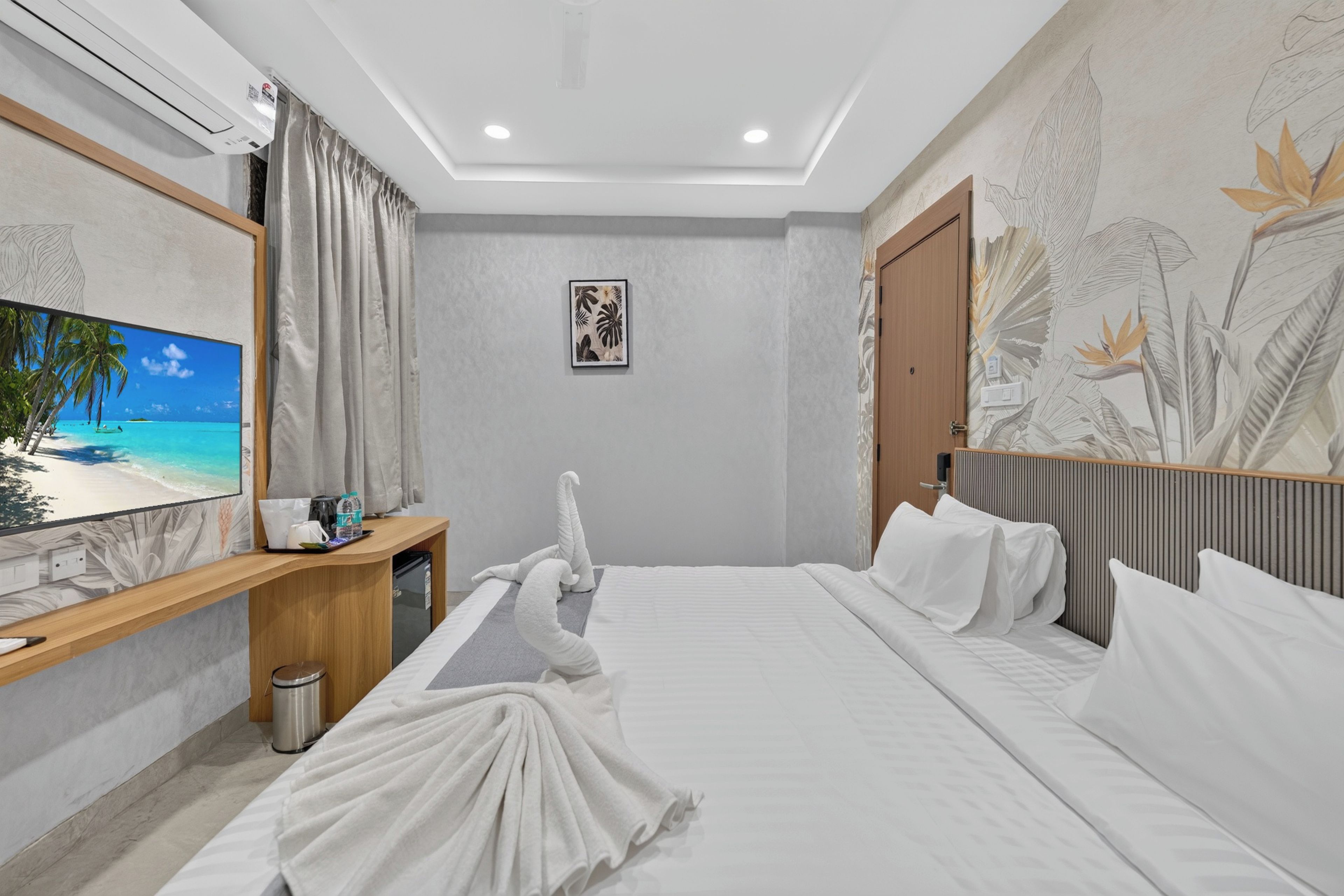 Een hotelkamer met een bed, een bureau, een prullenbak, een televisie en een muur met tropische behang.