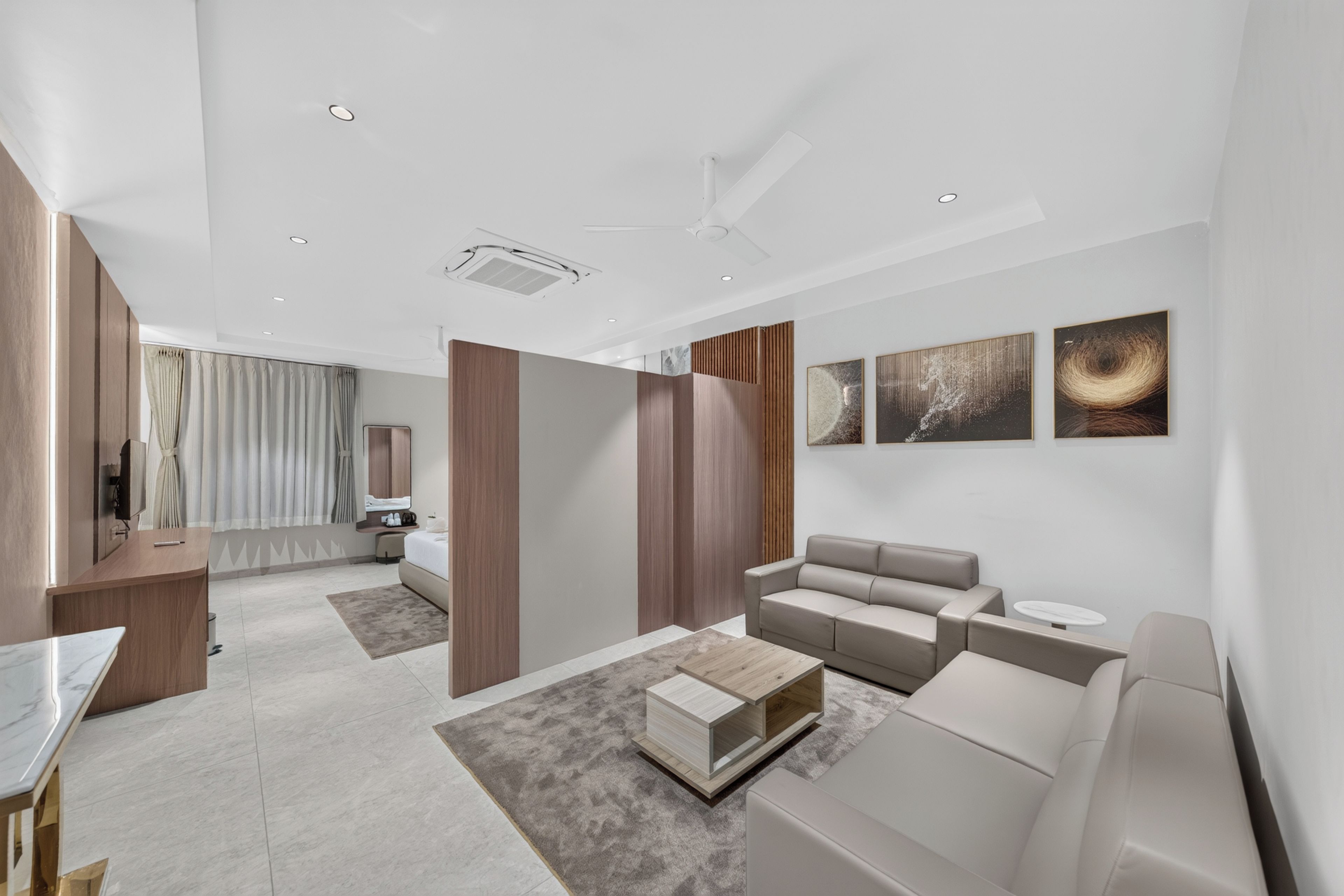 Habitación de hotel moderna con sofá, mesa de centro, televisor y baño visible a través de una separación.