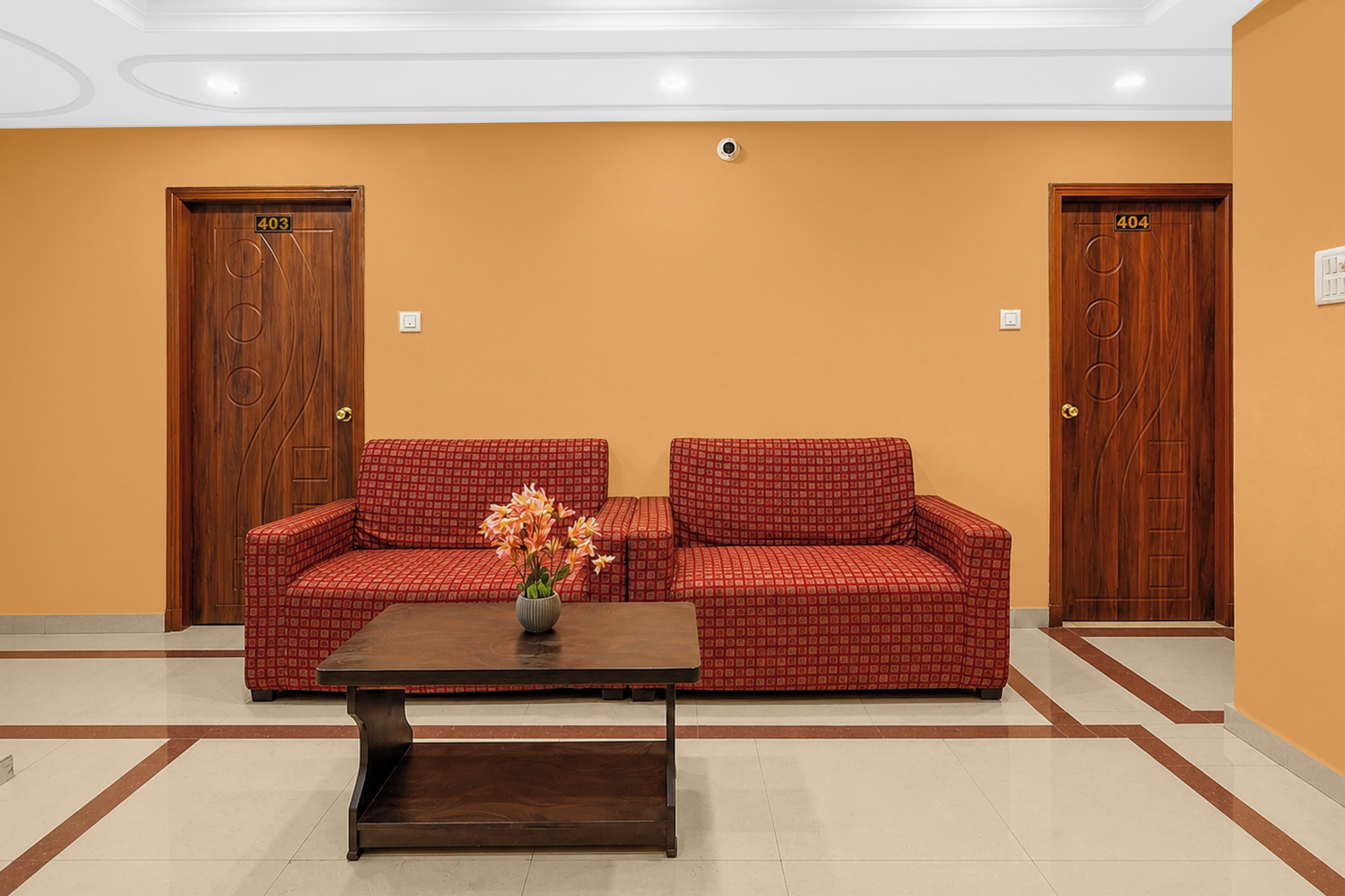 Ein Empfangsbereich mit einem roten, gemusterten Sofa, einem Holztisch mit Blumen und zwei Holztüren mit den Nummern 403 und 404.