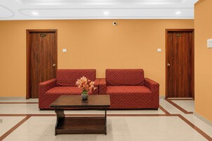 Un área de recepción con un sofá rojo estampado, una mesa de centro de madera con un jarrón de flores, y dos puertas de madera con los números 403 y 404.