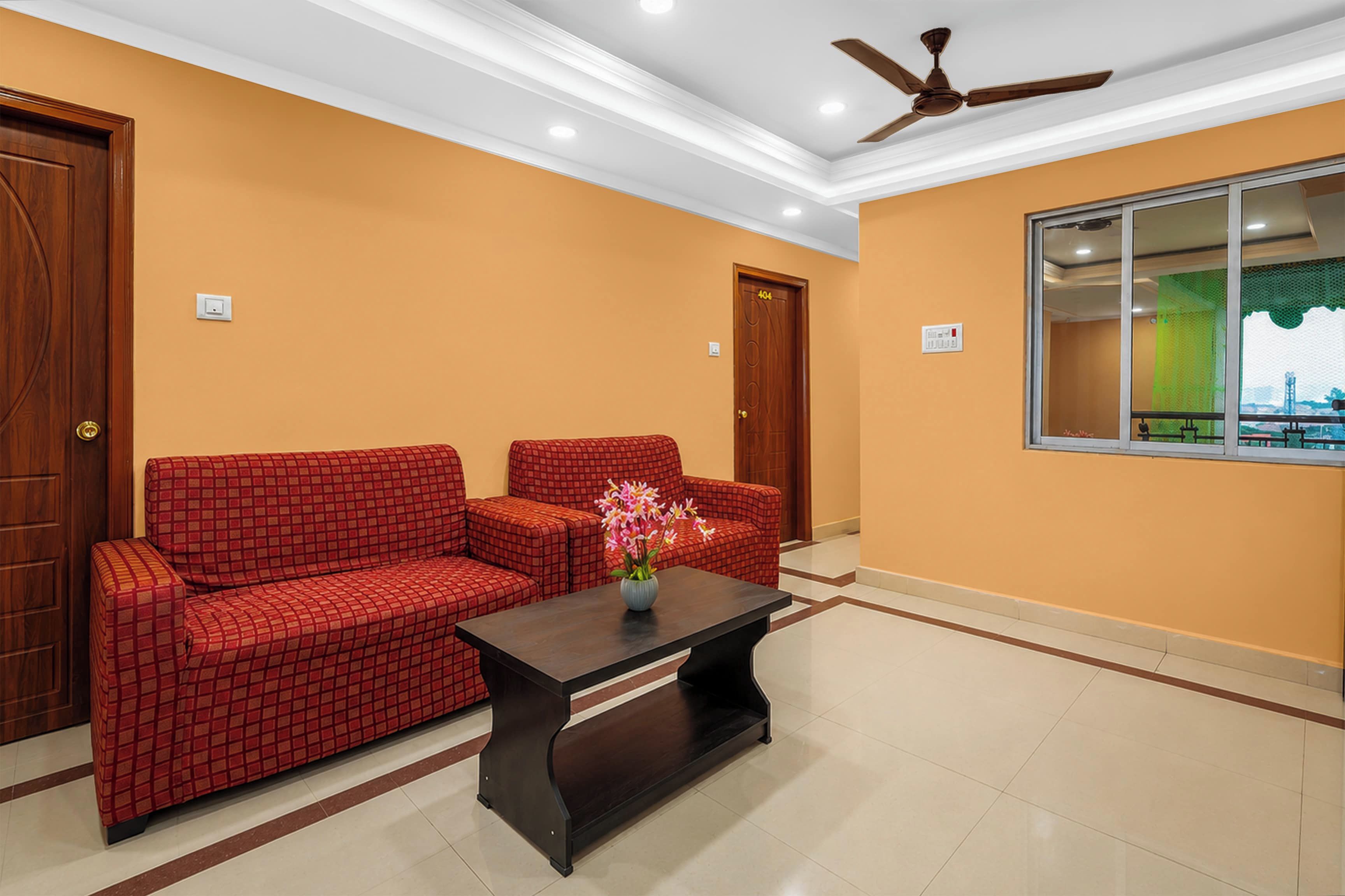 Una habitación con un sofá rojo a cuadros, una mesa de centro de madera oscura y un ventilador de techo.