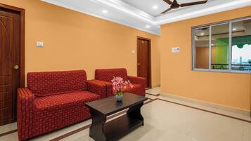 Una habitación con un sofá rojo a cuadros, una mesa de centro de madera oscura y un ventilador de techo.