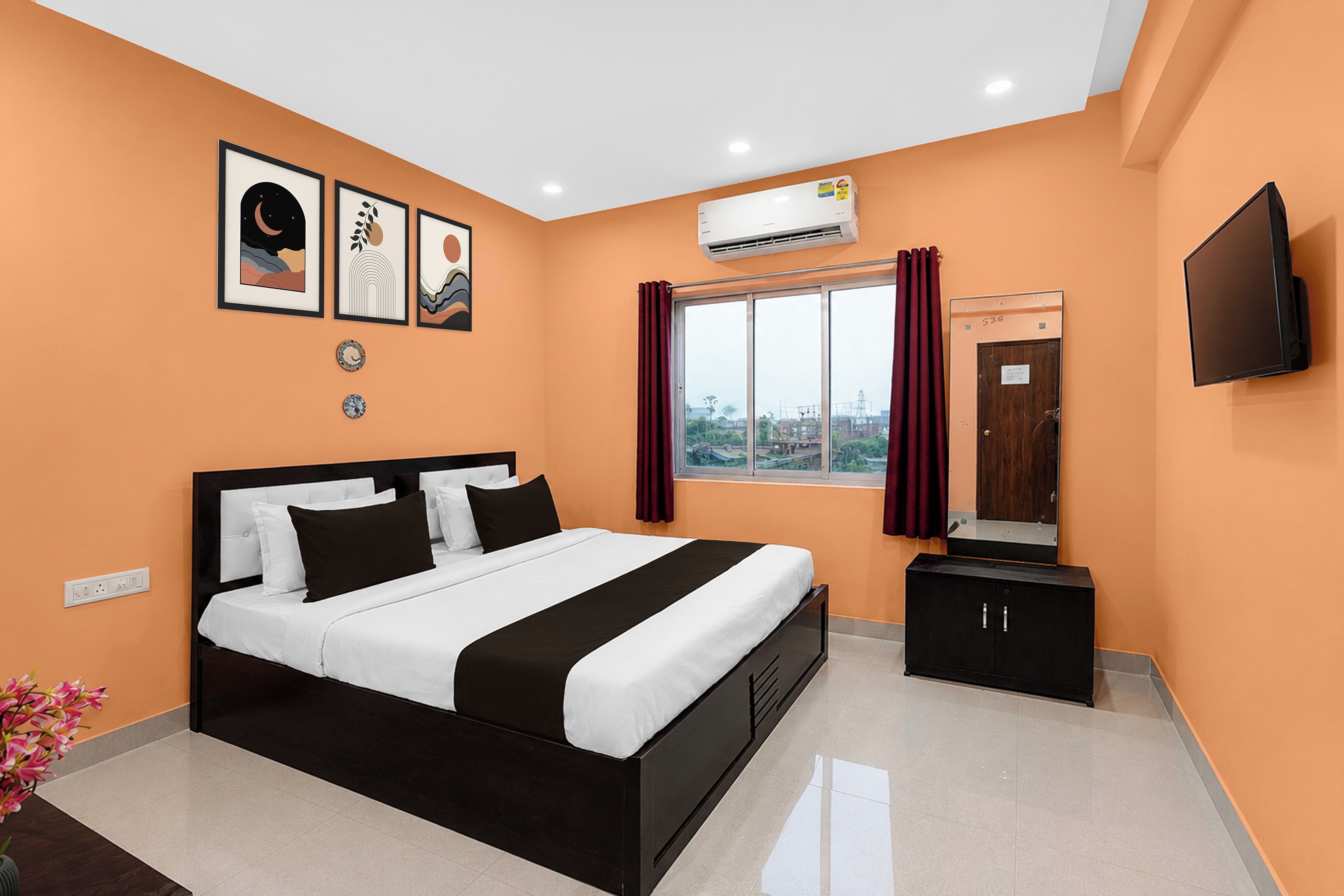 Habitación de hotel con cama, televisión, aire acondicionado, ventana con cortinas y obras de arte en la pared.