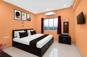 Habitación de hotel con cama, televisión, aire acondicionado, ventana con cortinas y obras de arte en la pared.