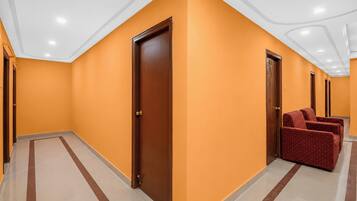 Un pasillo de hotel con paredes anaranjadas, puertas de madera y una zona de estar con sillones tapizados en rojo.