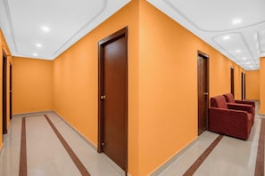 Un pasillo de hotel con paredes anaranjadas, puertas de madera y una zona de estar con sillones tapizados en rojo.