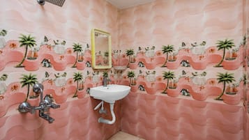A bathroom with a sink, mirror, and shower. The walls have a wavy pattern with palm trees and houses.