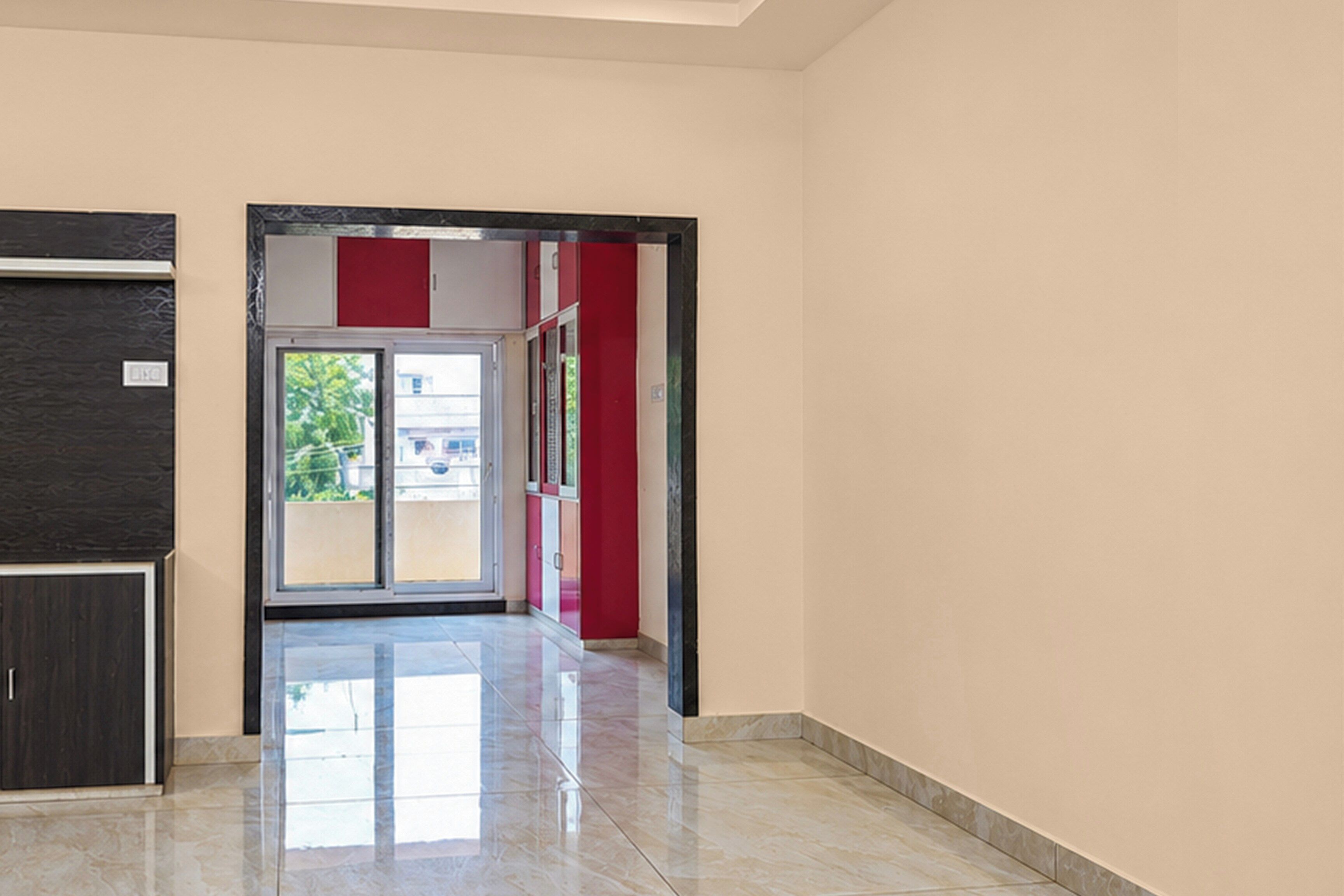 Un pasillo con una puerta que da a un espacio exterior, suelo de baldosas y una pared con detalles en rojo.