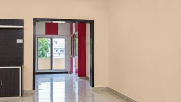 Un pasillo con una puerta que da a un espacio exterior, suelo de baldosas y una pared con detalles en rojo.