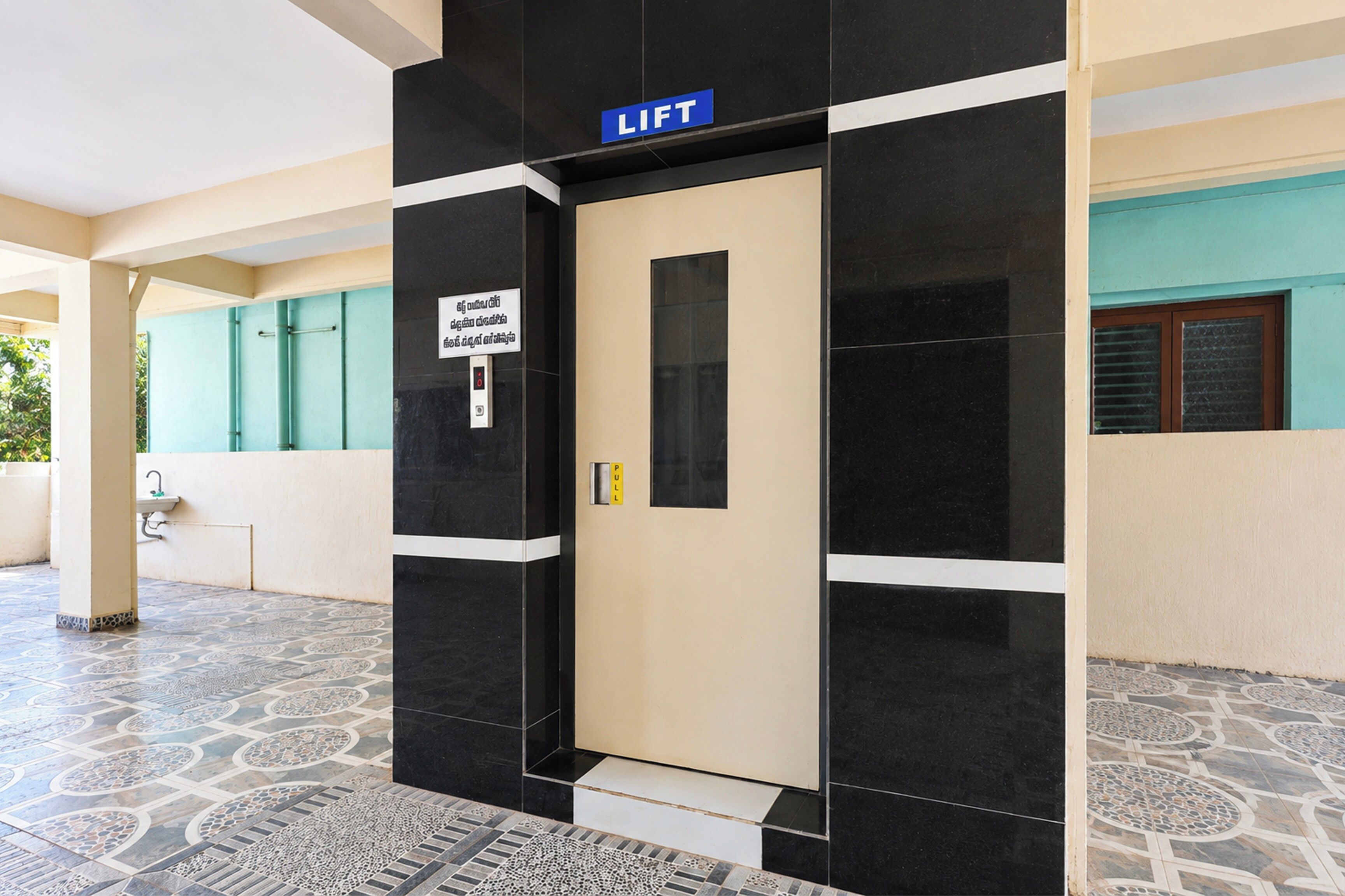 A lift door with a sign indicating a lift, a pull handle, and a floor with patterned tiles.