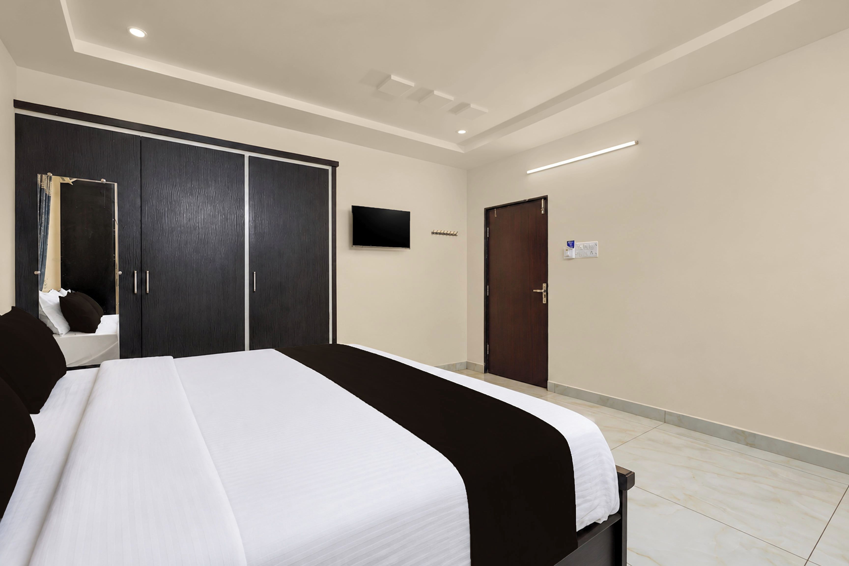 A hotel room with a large bed, a wardrobe, a television, and a door.