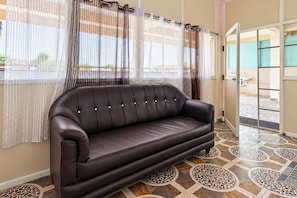 A dark brown leather sofa in a room with patterned floor tiles and sheer curtains with a geometric pattern. - Hotel O Achampeta Junction Kakinada (Kakinada)