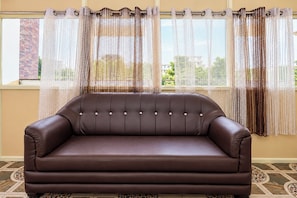 Un sofá de cuero marrón en una habitación con cortinas estampadas y vistas a edificios.