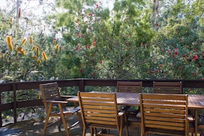 An outdoor seating area with wooden tables and chairs, surrounded by trees with red flowers and yellow foliage. - The Gap Escape - Retreat in the Trees (Halls Gap)