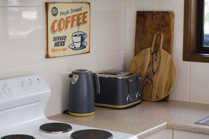 A kitchen with a coffee sign, a toaster, a kettle, and a wooden cutting board. - The Gap Escape - Retreat in the Trees (Halls Gap)
