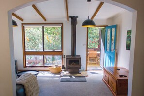A cozy room with a wood-burning stove, large windows, and a view of the outdoors. - The Gap Escape - Retreat in the Trees (Halls Gap)
