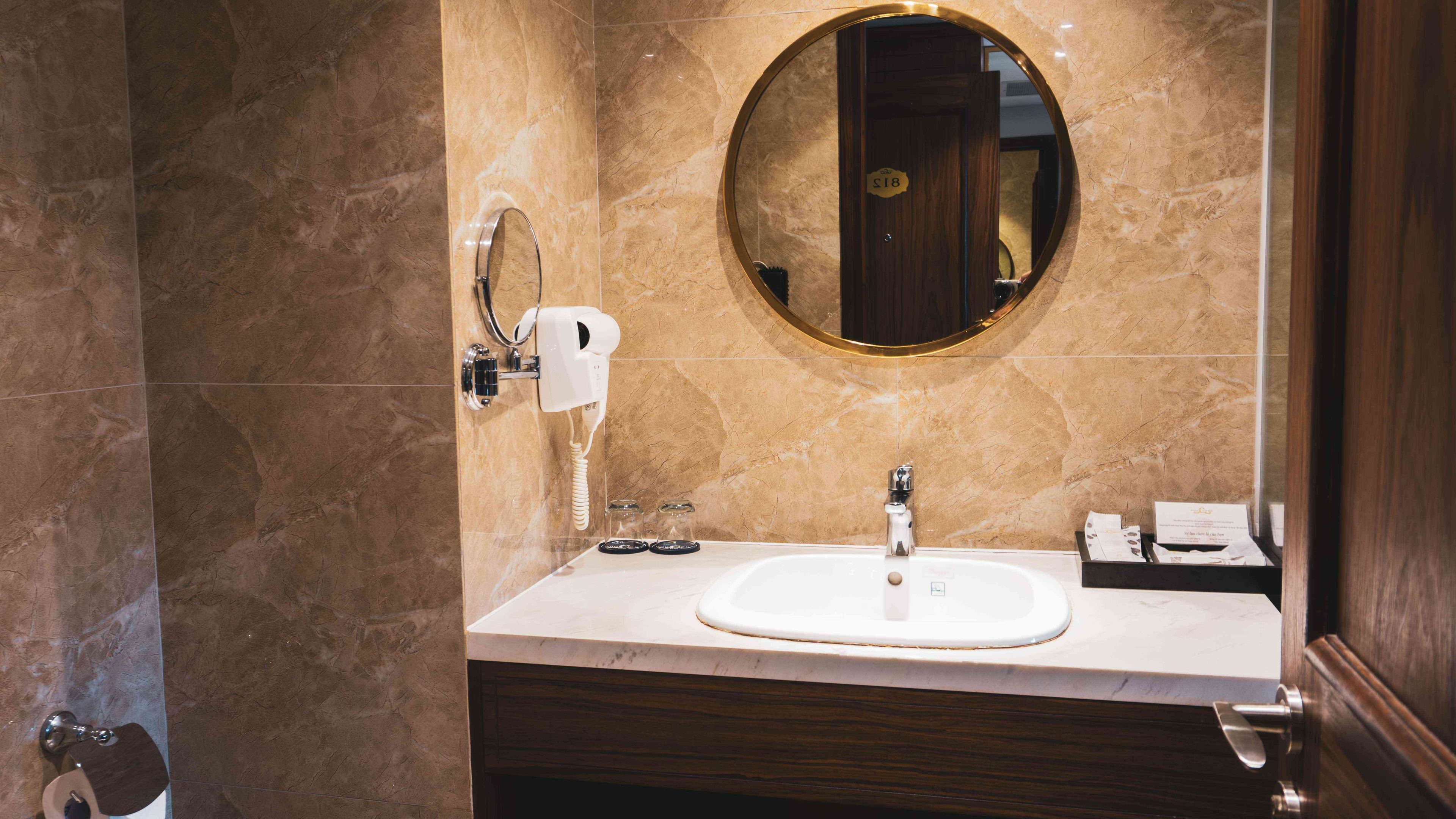 A bathroom with a marble wall, a round mirror, a sink, and a hairdryer.