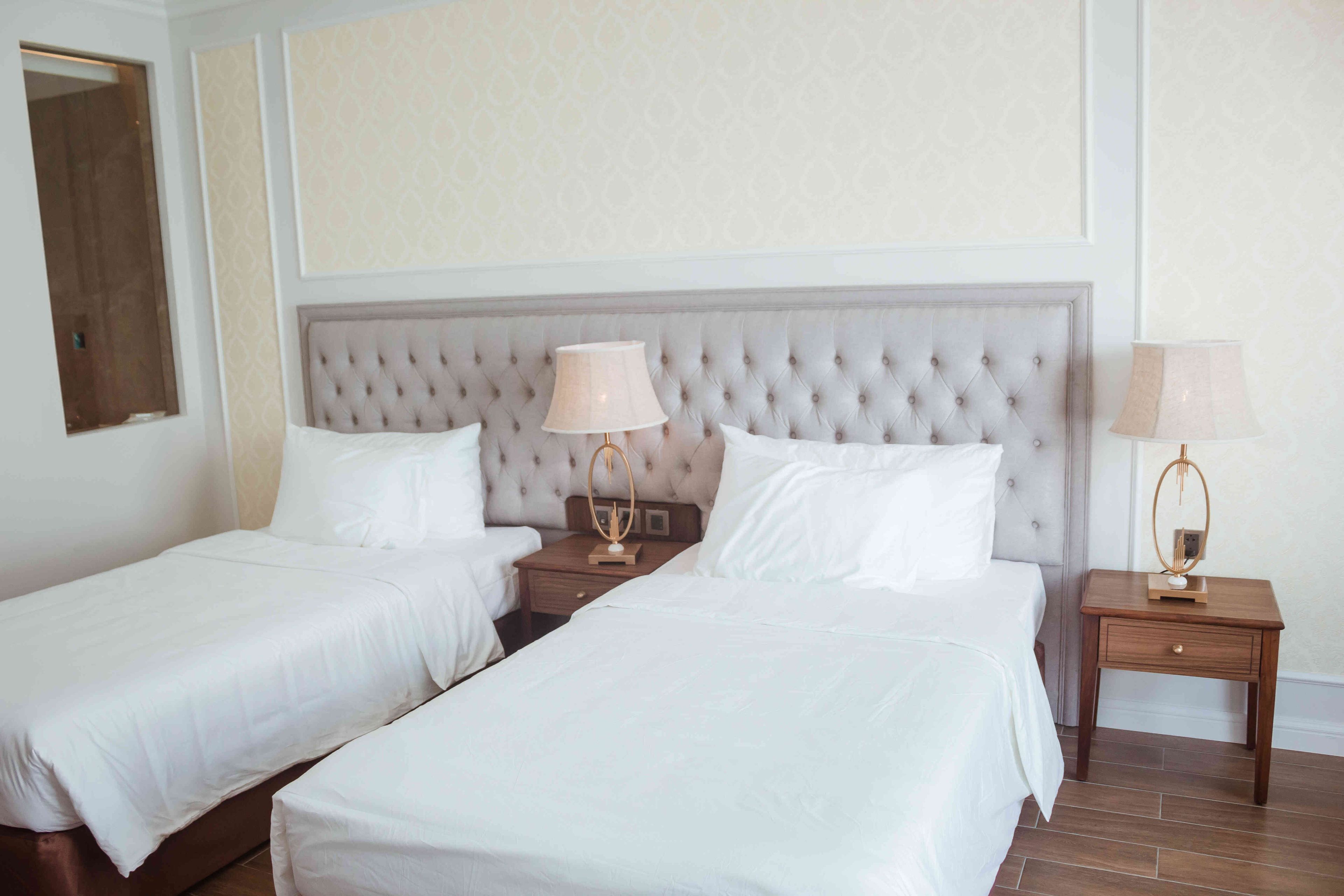 Una habitación de hotel con dos camas individuales, cada una con una mesita de noche de madera y una lámpara.