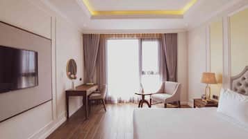 A hotel room with a bed, a desk, a chair, a TV, a bedside table with a lamp, and a window with curtains.