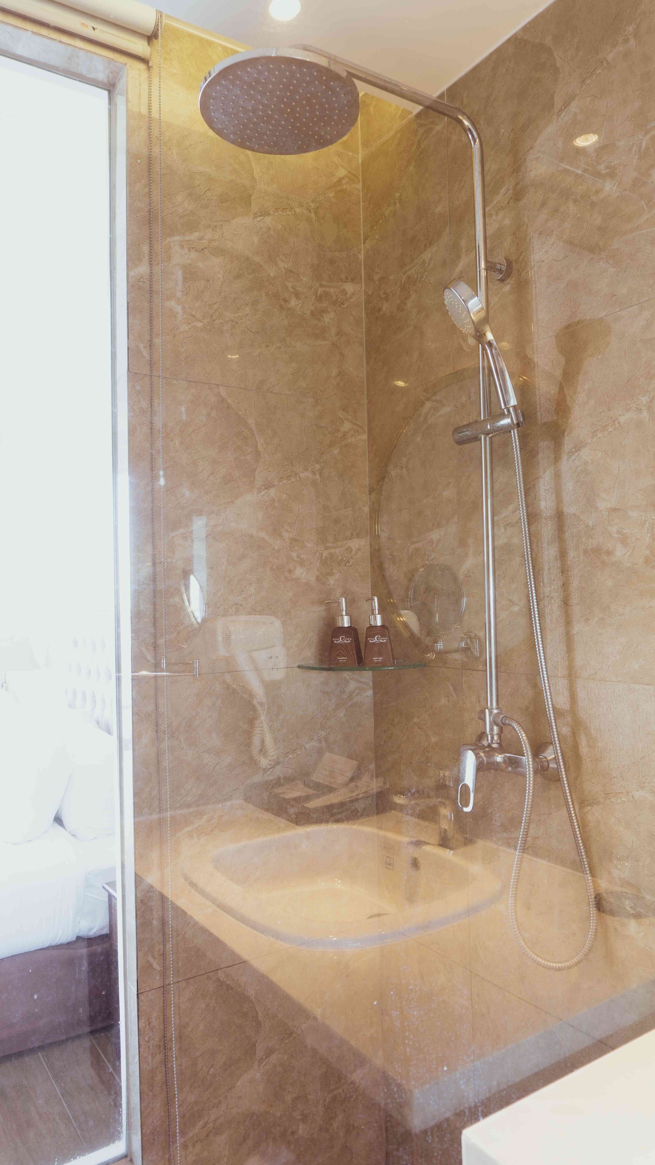 Ducha con mampara de vidrio, cabezal de ducha de mano y grifo empotrado.