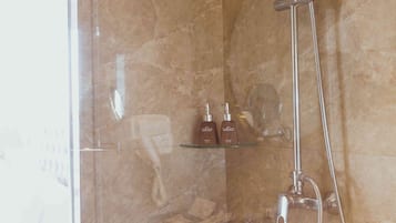 Ducha con mampara de vidrio, cabezal de ducha de mano y grifo empotrado.